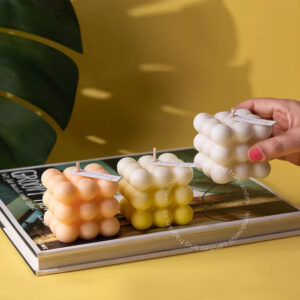 A hand places three bubble candles on a book titled "GROWTH" with a tropical plant leaf in the background, on a yellow surface.