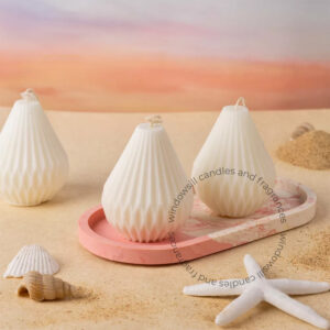 Three pear-shaped candles on a windowsill, accompanied by seashells and a sunset background.