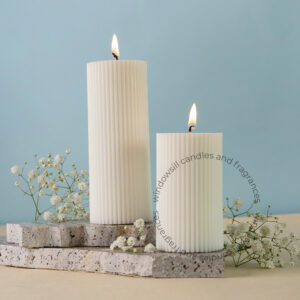 Two elegantly lit ribbed pillar candles set on concrete slabs with delicate baby's breath flowers in a glass vase on a soft blue background.