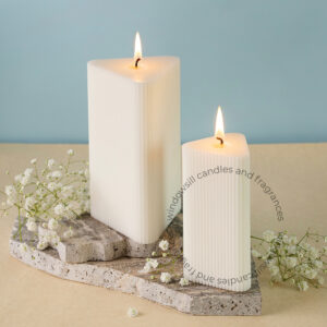 Two lit ribbed triangular pillar candles from Windowsill on a concrete candle holder with baby's breath flowers, showcasing a serene home decor setting