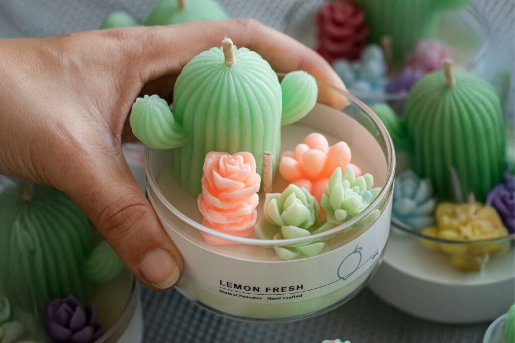 Handcrafted lemon fresh beeswax candle with cactus and floral designs in a glass jar, held by a hand, showcasing artisan quality.